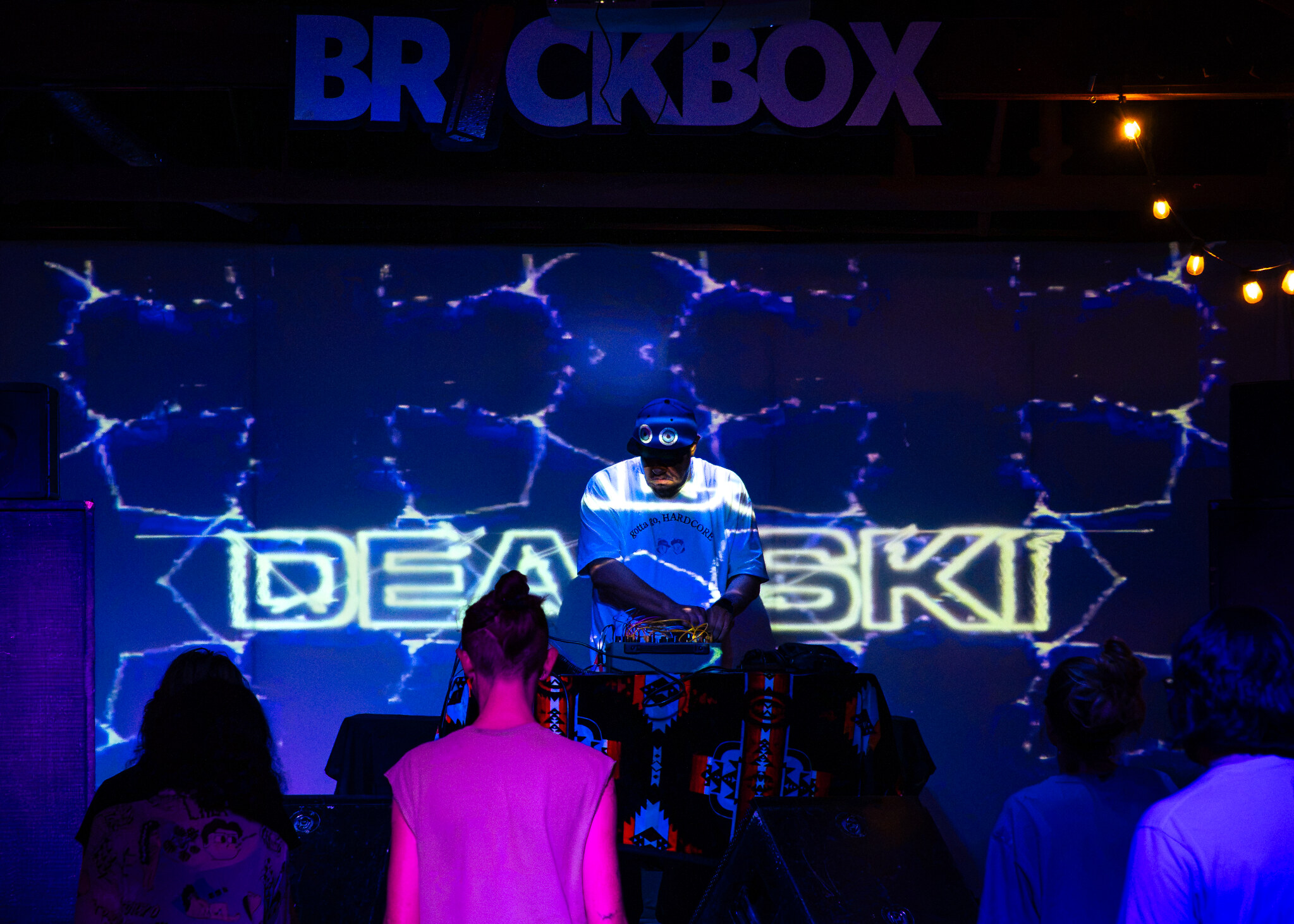 Deadski performing with hardware in front of his name projected on stage, with the audience in the foreground